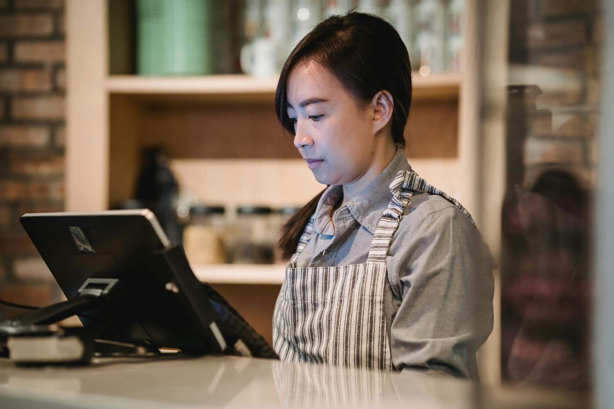 亞洲咖啡店店員在櫃台使用 POS 收銀系統處理訂單